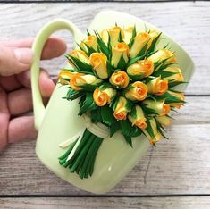 a hand holding a green coffee mug with yellow flowers in it and a person's hand next to it