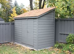 a gray shed sitting in the middle of a yard next to a fence and trees