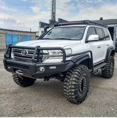 a white truck parked in front of a building with large tires on it's tires