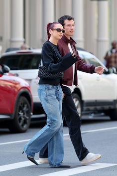 two people walking down the street in front of some cars and one is holding his arm out