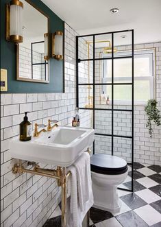 a white toilet sitting next to a sink in a bathroom under a mirror with gold fixtures