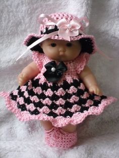 a baby doll wearing a pink and black crochet dress with matching hat, diaper and booties