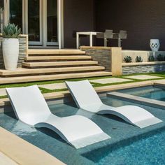 two white lounge chairs sitting next to a swimming pool in front of a large house