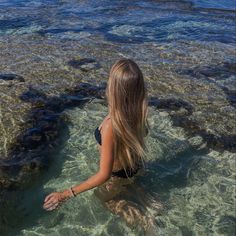 a woman is sitting in the water looking at the rocks and corals on the beach