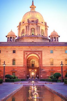 the front entrance to an old building with water fountain in foreground and lights on