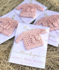 three pink crocheted baby sweaters on top of some white cards with thank you written on them