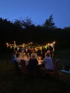 a group of people sitting around a dinner table with lights strung across the entire area