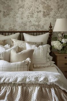 a bed with lots of pillows on top of it next to a night stand and lamp