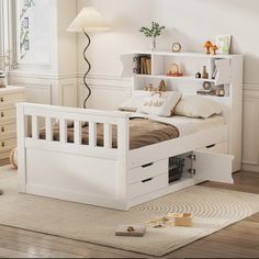 a white bed with drawers underneath it in a room next to a lamp and dresser