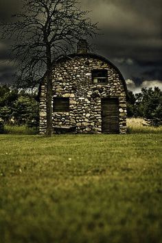 an old stone building with a tree in the foreground and dark clouds above it