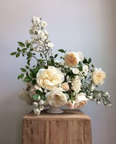 a vase filled with lots of white flowers on top of a wooden table next to a wall