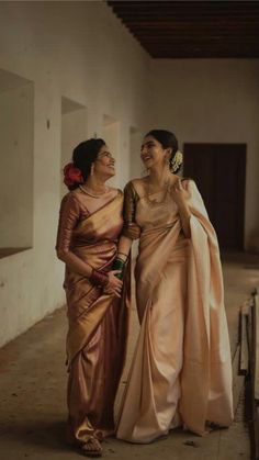 two women standing next to each other wearing sari and holding onto one another's hand