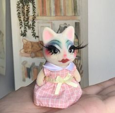 a hand holding a small toy cat with makeup on it's face and eyes