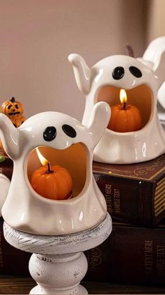 two white ceramic ghost candlestick holders with pumpkins in the middle on top of a stack of books