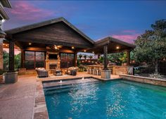 an outdoor kitchen and pool area at dusk with lights on the ceiling, grills in the background