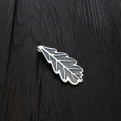 a silver leaf brooch sitting on top of a wooden table next to a black background