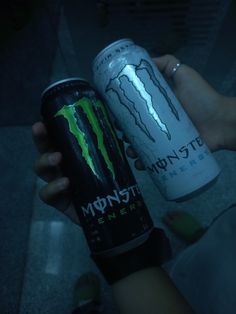 a person holding two cans of monster energy drink in their hands, both with lightning designs on them