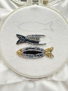 two fish on a white cloth with gold and silver beads in the hoop next to each other