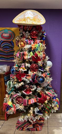 a decorated christmas tree in front of a purple wall with mexican hats on top and ribbons around it