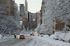 cars driving down a snow covered street with tall buildings in the backgrouds