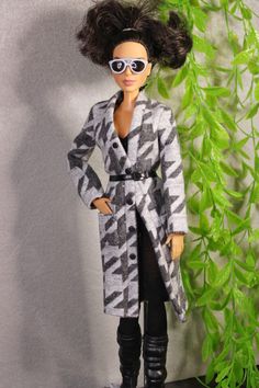 a barbie doll dressed in black and white with sunglasses on her head, standing next to a green plant