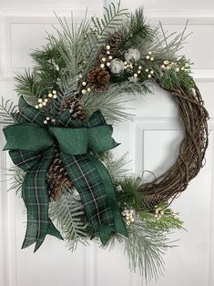 a wreath with pine cones and greenery hanging on a door