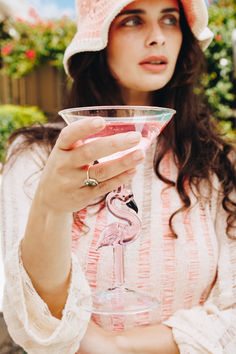 a woman wearing a pink hat holding a wine glass with a flamingo on it