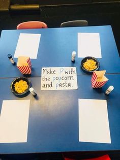 a blue table topped with plates of food and cups filled with popcorn next to a sign that says make p with the popcorn and pasta