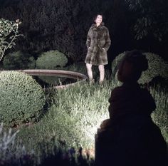 a man standing in the grass next to a small pond at night with his hands on his hips