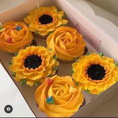 cupcakes with yellow frosting and sunflower decorations in a box on a table