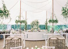 an outdoor wedding reception setup with white flowers and greenery on the tables, along with bar stools