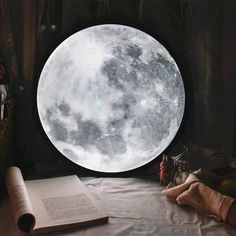 an open book sitting on top of a table next to a giant moon window with the moon in it