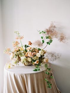 an arrangement of flowers sits on top of a round table in front of a white wall