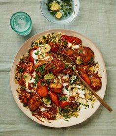 a white plate topped with lots of food next to a bowl of salad and a glass of water