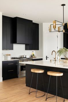 a kitchen with black cabinets and white counter tops, gold pendant lights over the island