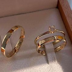 two gold wedding rings sitting on top of a white cloth next to an open box