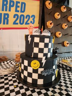 a black and white checkered cake with yellow smiley faces on the top is surrounded by donuts