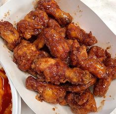 a white plate topped with chicken wings covered in sauce next to a bowl of ketchup