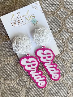 two white and pink earrings sitting on top of a piece of paper next to a card