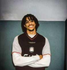 a young man with his arms crossed standing in front of a wall wearing a football uniform