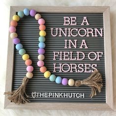 a wooden sign that says be a unicorn in a field of horses with beads and tassels