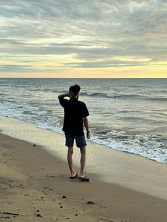 a man standing on top of a sandy beach next to the ocean under a cloudy sky