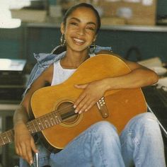 a woman sitting in a chair holding an acoustic guitar and smiling at the camera with her arms crossed