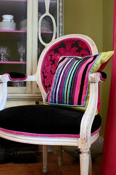 a chair with colorful pillows on it in front of a book shelf and china cabinet