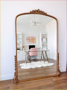 a large gold mirror sitting on top of a hard wood floor next to a desk