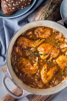 a pan filled with chicken and gravy on top of a wooden cutting board