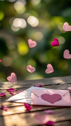 a pink envelope with hearts flying out of it on top of a wooden table surrounded by petals