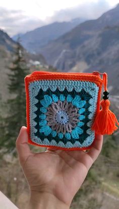 a hand holding up a crocheted square with an orange tassel