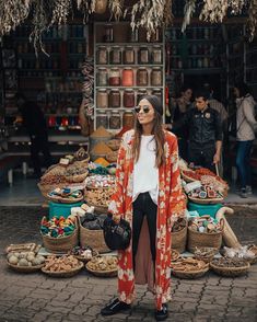 a woman standing in front of a market with lots of baskets and food on display