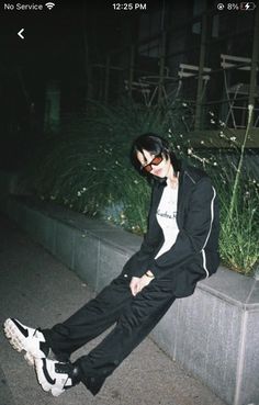 a young man sitting on the side of a cement wall next to a planter